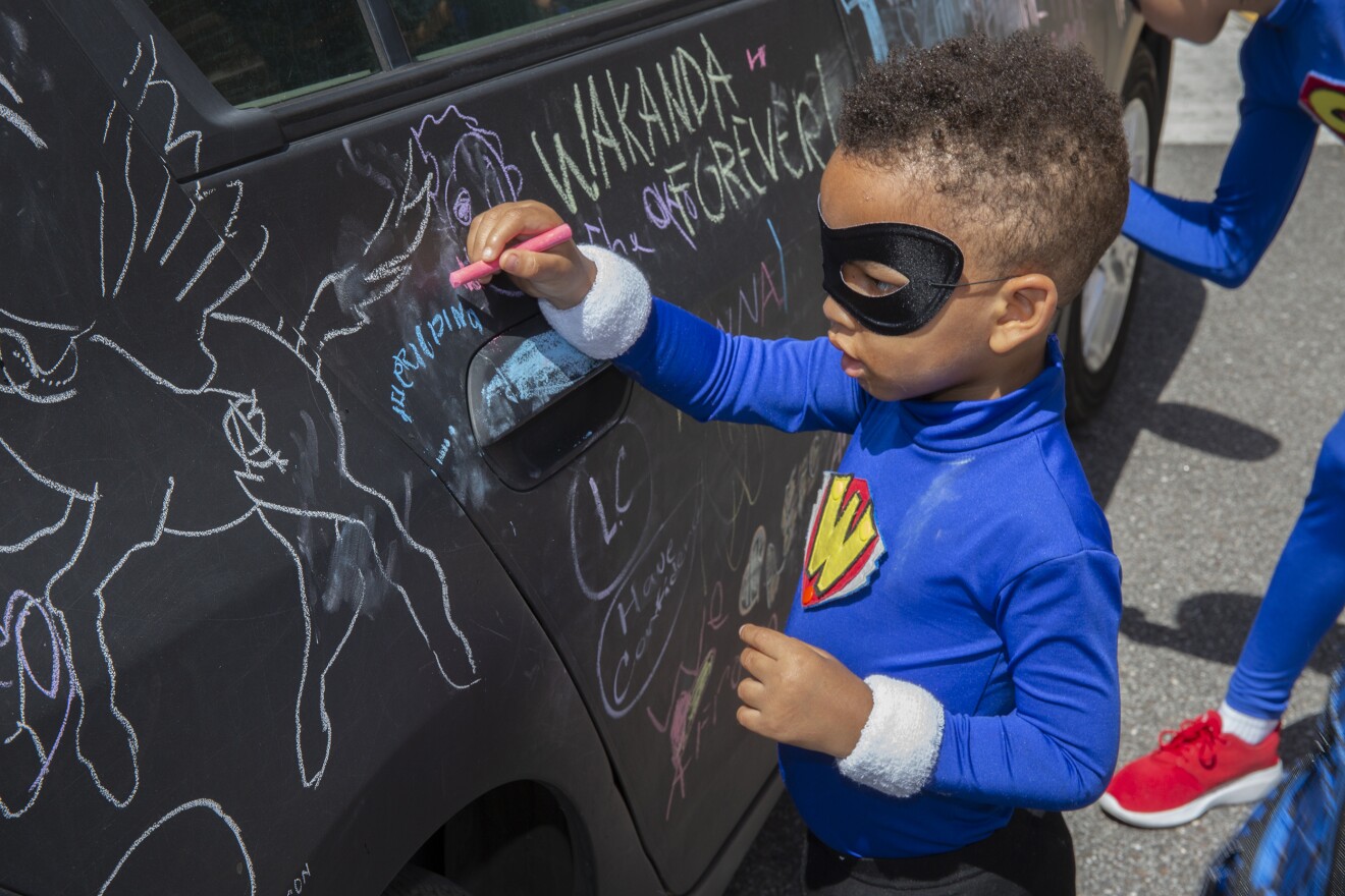 A little superhero writes on the chalkboard car outside the library at AfroCon.